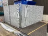 A tall galvanized chain-link security enclosure with gray privacy slats protecting outdoor industrial equipment