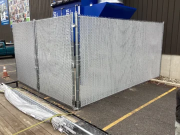 A tall galvanized chain-link security enclosure with gray privacy slats protecting outdoor industrial equipment