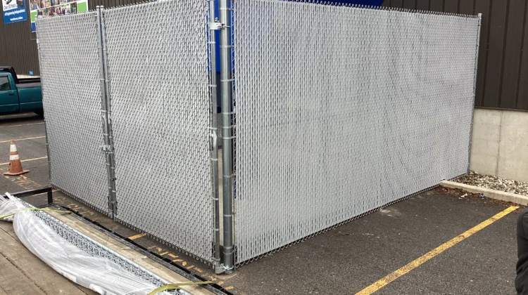 A tall galvanized chain-link security enclosure with gray privacy slats protecting outdoor industrial equipment