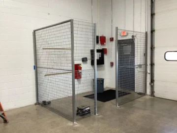 An indoor industrial security cage made of silver welded wire mesh with a double-gated entrance