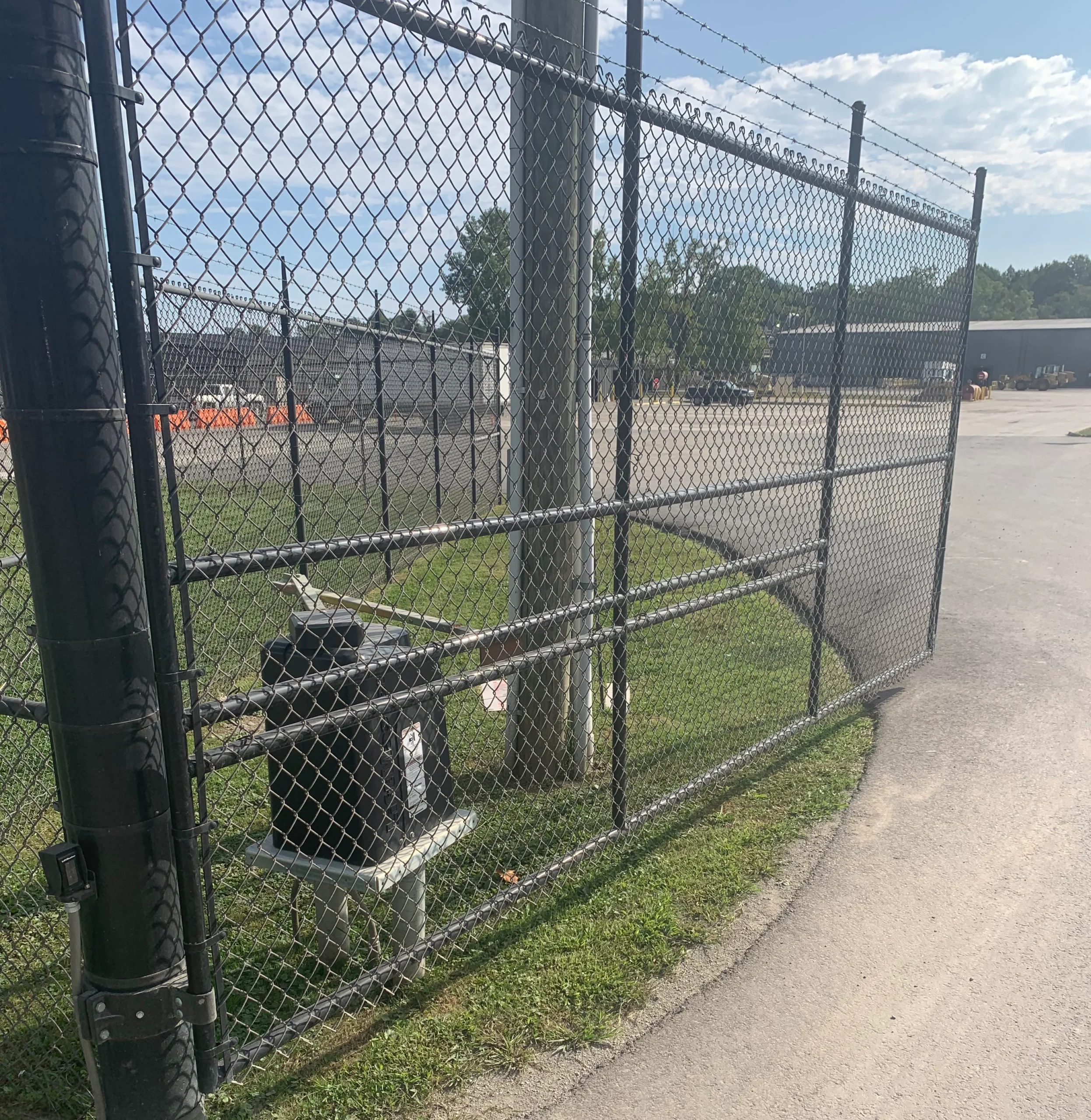 Black chain-link security fence with a barbed-wire topper and an automatic gate operator